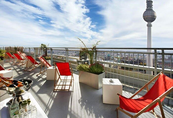 Rooftop view at Park Inn by Radisson Berlin Alexanderplatz, a gay-friendly hotel. Red lounge chairs, drinks, and the TV tower in the background.