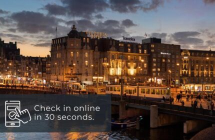 Park Plaza Victoria Amsterdam Hotel at dusk. Gay-friendly hotel with trams, bridge, and waterfront view. Check in online in 30 seconds.