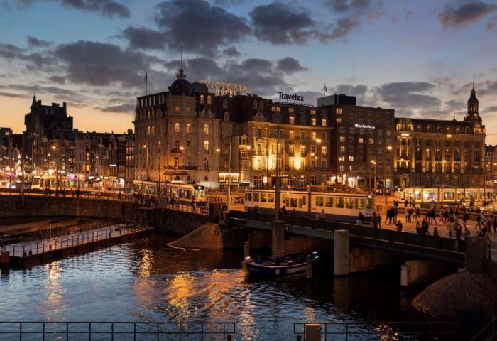 Park Plaza Victoria Amsterdam Hotel at dusk. Cityscape view of the gay-friendly hotel with canal, trams, and people. Amsterdam travel.