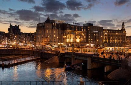 Park Plaza Victoria Amsterdam Hotel at dusk. Cityscape view of the gay-friendly hotel with canal, trams, and people. Amsterdam travel.