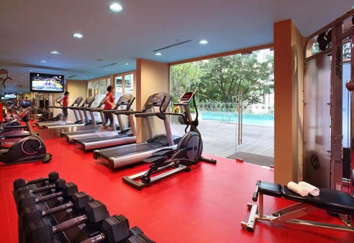 Park Regis Singapore gay-friendly hotel gym. Treadmills, weights, and exercise equipment on a red floor. Pool view. Fitness for gay travelers.