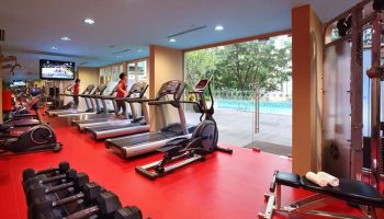 Park Regis Singapore gay-friendly hotel gym. Treadmills, weights, and exercise equipment on a red floor. Pool view. Fitness for gay travelers.