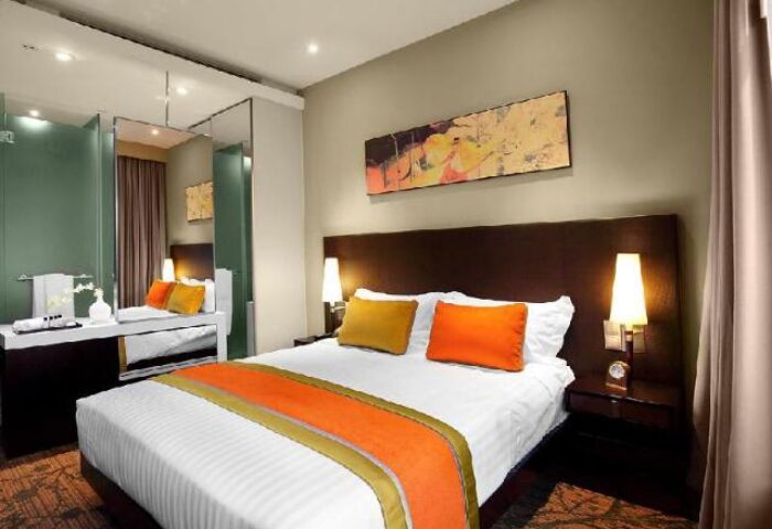 Park Regis Singapore gay-friendly hotel room. Modern design, queen bed with orange accents, bathroom with glass partition.