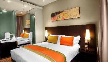 Park Regis Singapore gay-friendly hotel room. Modern design, queen bed with orange accents, bathroom with glass partition.