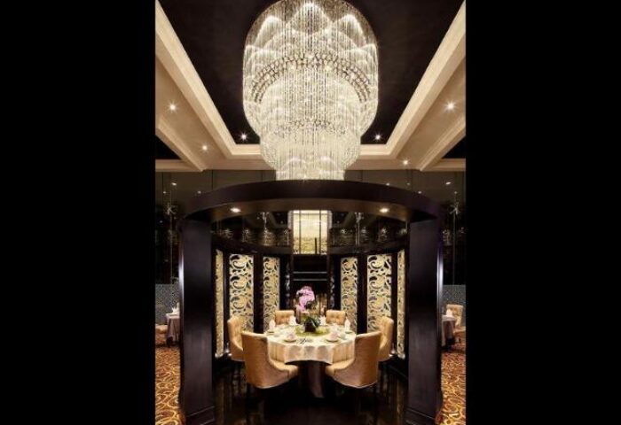 Dining area at Park Regis Singapore, a gay-friendly hotel. Features round table, chairs, ornate chandelier, and decorative screens.