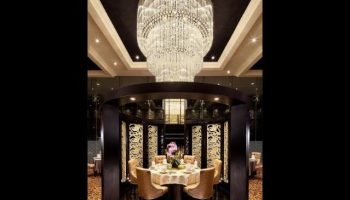 Dining area at Park Regis Singapore, a gay-friendly hotel. Features round table, chairs, ornate chandelier, and decorative screens.
