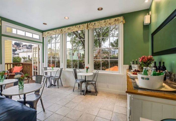 Parker Guest House's sunroom with tables, chairs, and a view. This gay-friendly hotel provides a welcoming space for relaxation and socializing.