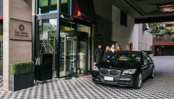 Exterior of the gay-friendly Parker Hotel Vancouver, showcasing the entrance with a revolving door, a black car, and guests arriving.