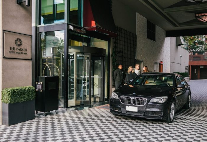 Exterior of the gay-friendly Parker Hotel Vancouver, showcasing the entrance with a revolving door, a black car, and guests arriving.