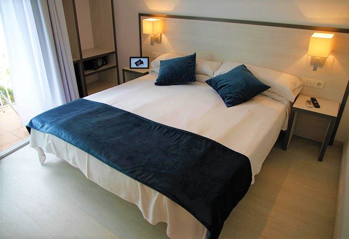 Parrots Sitges Hotel: Gay-friendly hotel room with double bed, blue cushions and bed runner. Balcony and bedside table. Gay travel advice.