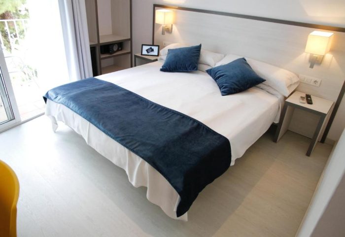 Parrots Sitges Hotel room. Gay-friendly hotel with a double bed, blue pillows and bed runner. Nightstand and lamps. Modern decor.