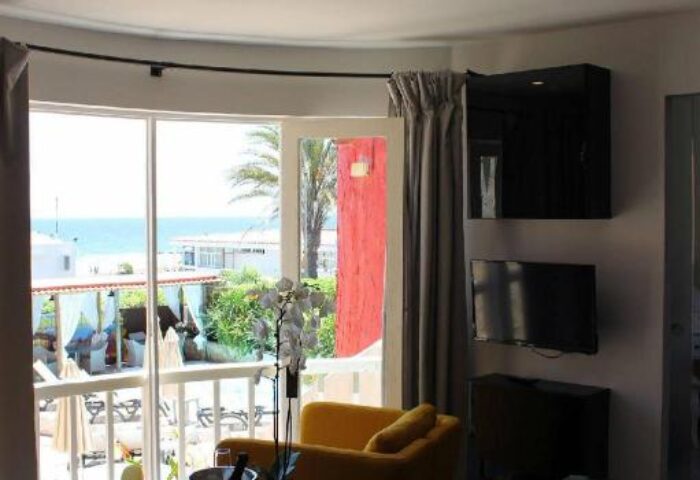 Pasion Tropical Gay Only Resort suite interior. View of balcony, ocean, yellow chairs, and table. Gay-friendly hotel room.