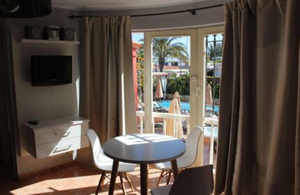 Pasion Tropical Gay Only Resort room. Interior view with table, chairs, TV, and balcony overlooking the pool. Gay-friendly hotel.