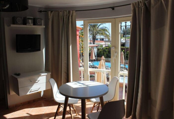 Pasion Tropical Gay Only Resort room. Interior view with table, chairs, TV, and balcony overlooking the pool. Gay-friendly hotel.