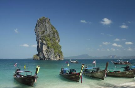 Peace Laguna Resort's beach view. Longtail boats on the shore, rock formation in the sea. Gay-friendly hotel travel destination.
