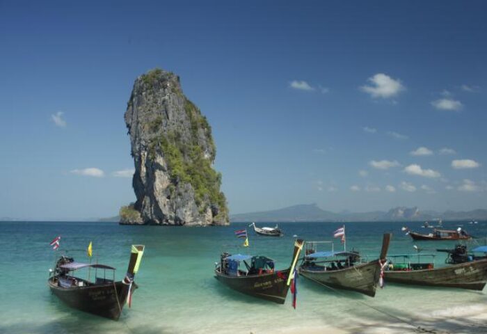 Peace Laguna Resort's beach view. Longtail boats on the shore, rock formation in the sea. Gay-friendly hotel travel destination.