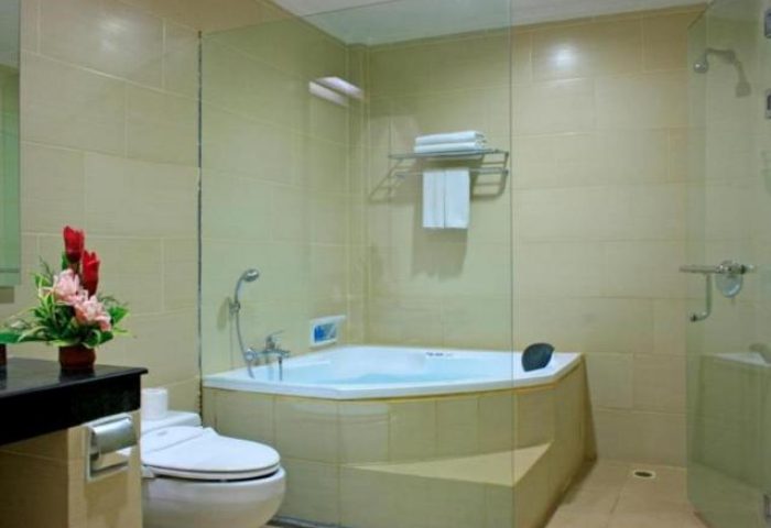 Bathroom at Gay-Friendly Pelangi Bali Hotel & Spa. Bathtub, toilet, and shower behind glass. Flowers add a nice touch to this Bali hotel.