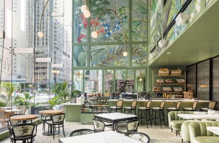 Pendry Chicago's gay-friendly hotel interior. A stylish cafe with green walls, floral murals, and modern lighting. Tables and chairs for guests.
