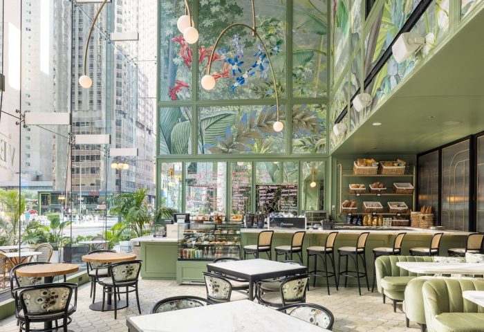 Pendry Chicago's gay-friendly hotel interior. A stylish cafe with green walls, floral murals, and modern lighting. Tables and chairs for guests.