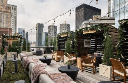Pendry Chicago gay-friendly hotel rooftop bar. Outdoor lounge with city views, string lights, wooden chairs, and Fever-Tree signage.