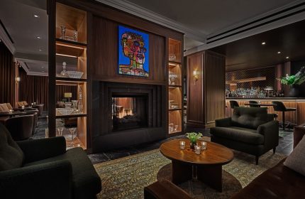 Pendry Chicago, a gay-friendly hotel. Interior view of the bar and lounge area with a fireplace, seating, and bar. Upscale and inviting.
