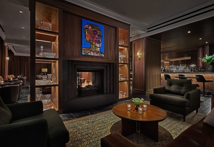Pendry Chicago, a gay-friendly hotel. Interior view of the bar and lounge area with a fireplace, seating, and bar. Upscale and inviting.