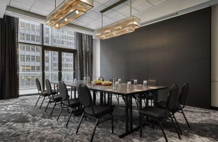 Pendry Chicago gay-friendly hotel meeting room. Table with chairs, glasses, fruit. Large window with city view. Modern lighting.