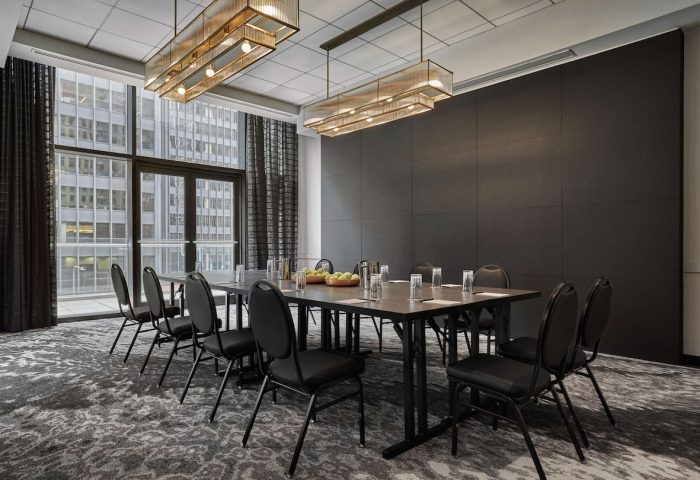 Pendry Chicago gay-friendly hotel meeting room. Table with chairs, glasses, fruit. Large window with city view. Modern lighting.