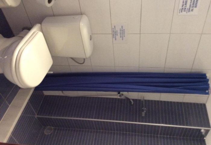Bathroom at Pension Ageliki Kalogera, a gay-friendly hotel. Toilet, shower with blue curtain, and tiled walls. Clean and simple design.