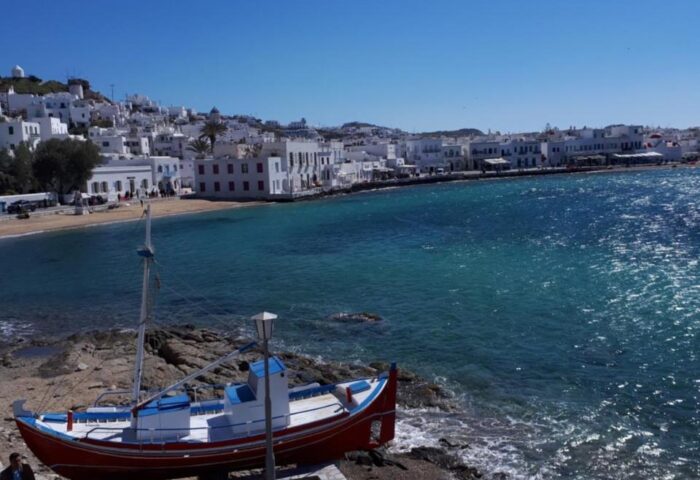 Gay-Friendly Hotel Pension Ageliki Kalogera view. A red and blue boat on the coast, with the town and sea in the background. Mykonos gay travel.