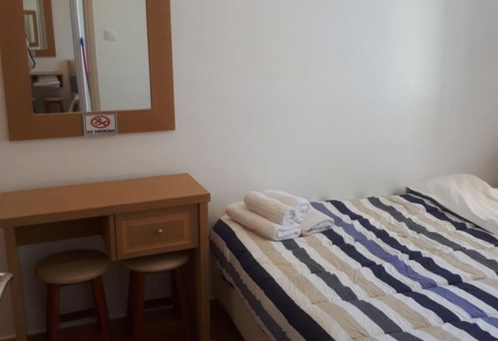 Pension Ageliki Kalogera room. Gay-friendly hotel featuring a bed with striped bedding, a vanity with mirror, and two stools.