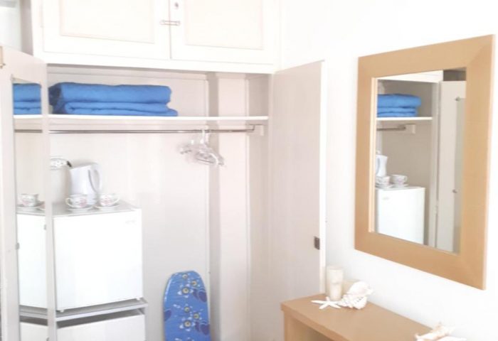 Pension Ageliki Kalogera gay-friendly hotel room. Interior with closet, mini fridge, blue towels, vanity, mirror, stool, and beach decor.