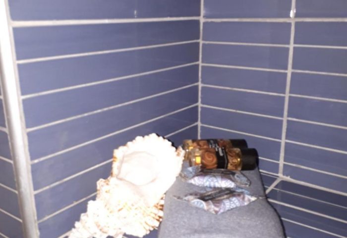 Gay-friendly Pension Ageliki Kalogera bathroom detail. Blue tiled wall with rolled towel, toiletries, condom and seashell.