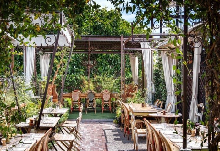 Petit Ermitage Hotel's outdoor dining area. Gay-friendly, adults-only hotel with lush greenery, tables, and chairs. Ideal for gay travelers.