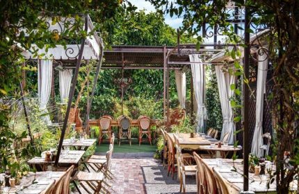 Petit Ermitage Hotel's outdoor dining area. Gay-friendly, adults-only hotel with lush greenery, tables, and chairs. Ideal for gay travelers.