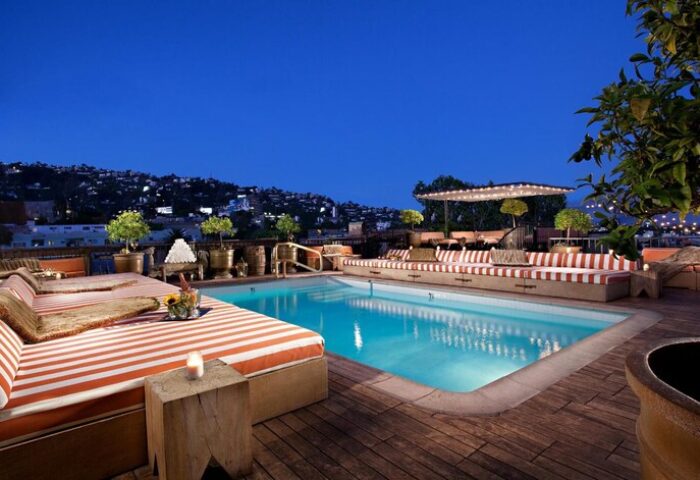 Petit Ermitage Hotel Adults-Only rooftop pool at night. Gay-friendly hotel with striped daybeds and city views. Perfect for gay travel.