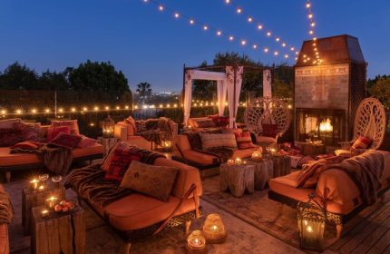 Petit Ermitage Hotel adults-only rooftop terrace at dusk. Cozy seating, fireplace, and string lights create a romantic, gay-friendly ambiance.