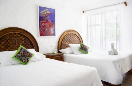 Petit Hotel Pilitas gay-friendly room. Two beds with patterned headboards, colorful pillows, and a vibrant painting. Bright, welcoming space.
