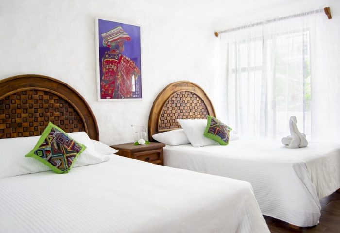 Petit Hotel Pilitas gay-friendly room. Two beds with patterned headboards, colorful pillows, and a vibrant painting. Bright, welcoming space.