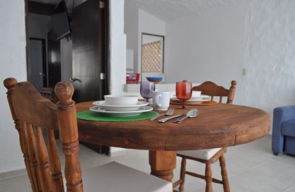 Petit Hotel Pilitas's dining area. Round wooden table set for a meal with plates, glasses, and cutlery. Gay-friendly hotel interior.