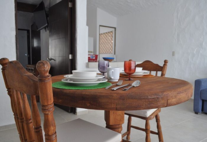 Petit Hotel Pilitas's dining area. Round wooden table set for a meal with plates, glasses, and cutlery. Gay-friendly hotel interior.