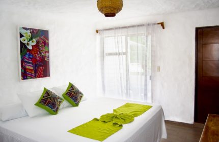 Petit Hotel Pilitas gay-friendly hotel room. White walls, bed with green accents, colorful artwork. Comfy, stylish gay travel lodging.