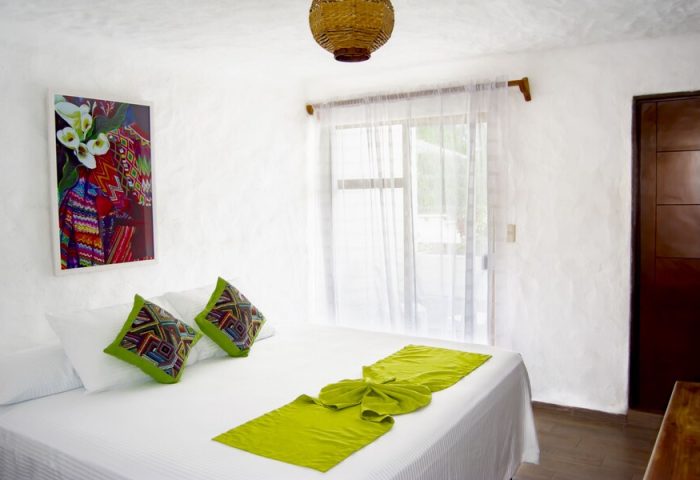 Petit Hotel Pilitas gay-friendly hotel room. White walls, bed with green accents, colorful artwork. Comfy, stylish gay travel lodging.