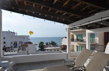 View from Petit Hotel Pilitas, a gay-friendly hotel. Deck chairs overlook the ocean. Parasailing in the distance. Travel advice.