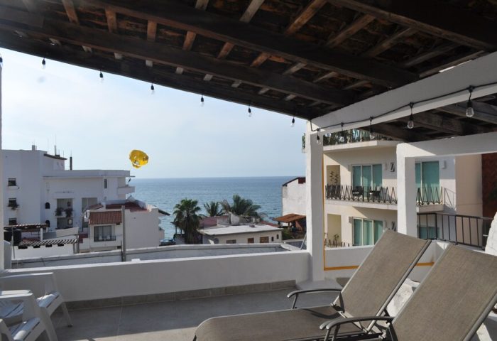 View from Petit Hotel Pilitas, a gay-friendly hotel. Deck chairs overlook the ocean. Parasailing in the distance. Travel advice.