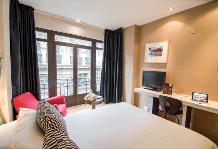 Petit Palace Chueca gay-friendly hotel room. Balcony view, desk, and modern decor. Ideal for gay travelers in Madrid's Chueca district.