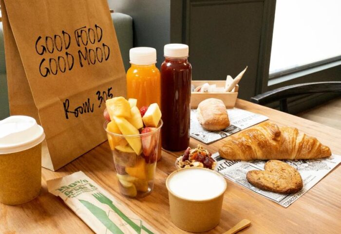 Petit Palace Chueca gay-friendly hotel breakfast. Room service with juice, fruit, croissant, yogurt, and coffee on a wooden table.