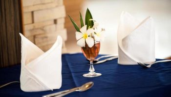 Table setting at Phi Phi Island Cabana Hotel. Flowers in glass, folded napkins, silverware on blue tablecloth. Gay-friendly hotel dining.