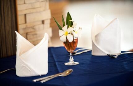 Table setting at Phi Phi Island Cabana Hotel. Flowers in glass, folded napkins, silverware on blue tablecloth. Gay-friendly hotel dining.