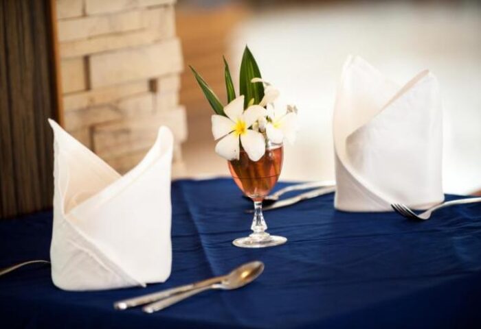 Table setting at Phi Phi Island Cabana Hotel. Flowers in glass, folded napkins, silverware on blue tablecloth. Gay-friendly hotel dining.